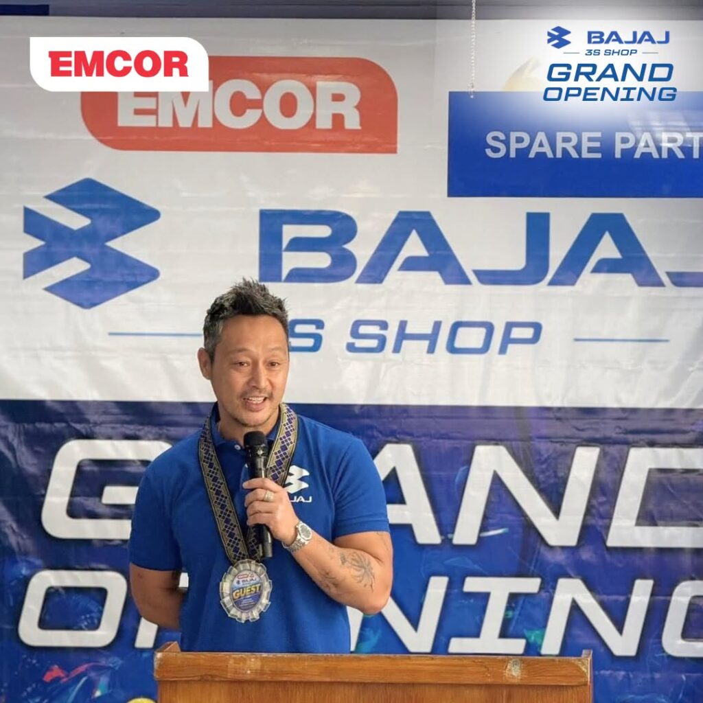 Guest in a blue shirt speaking into a microphone in front of the Bajaj 3S Shop backdrop