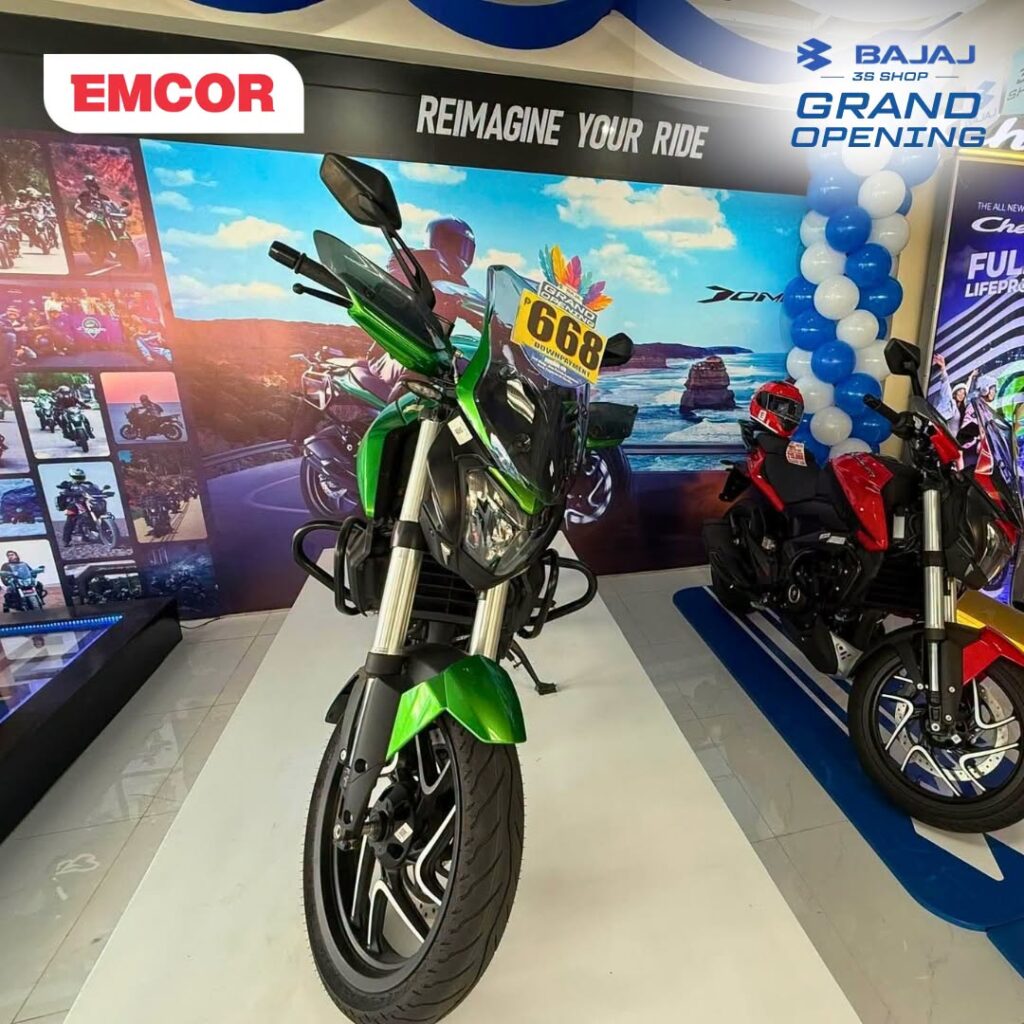 Green Bajaj Dominar motorcycle on display in the showroom, with another motorcycle and a Dominar backdrop behind it