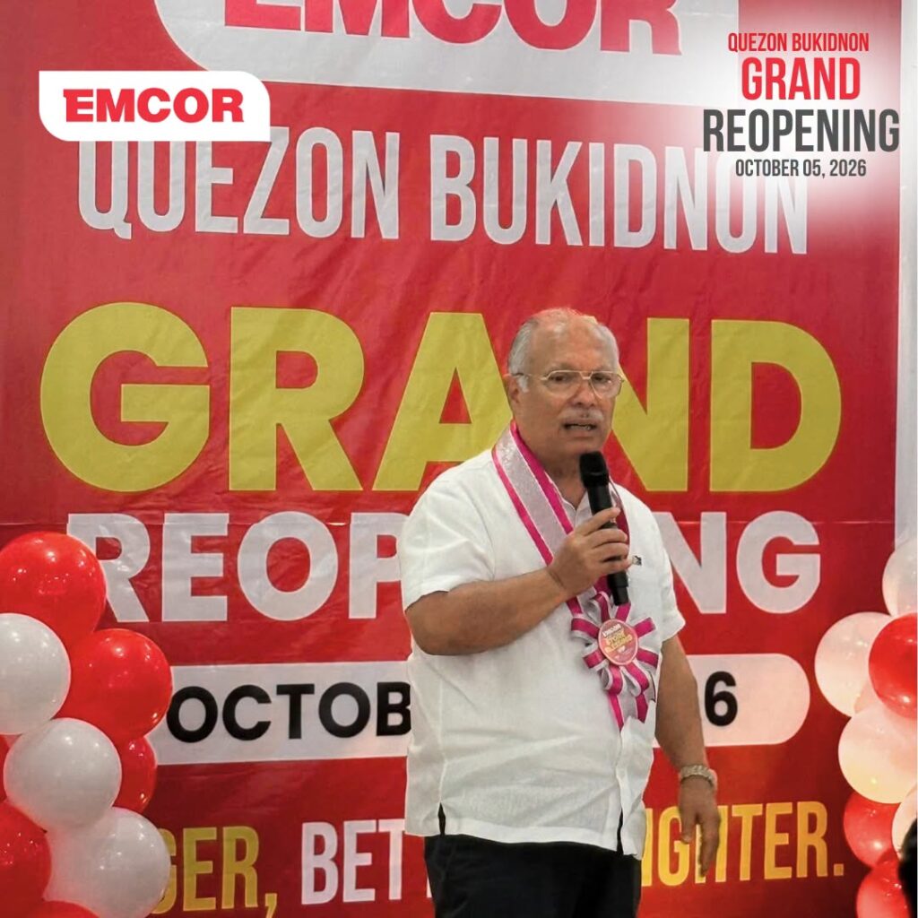 Guest in a white shirt and sash speaking into a microphone beside red and white balloons